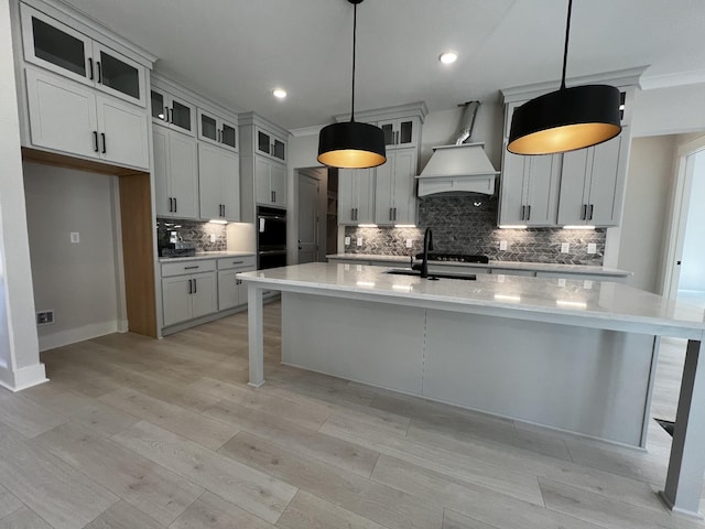 kitchen featuring custom exhaust hood, an island with sink, sink, hanging light fixtures, and ornamental molding