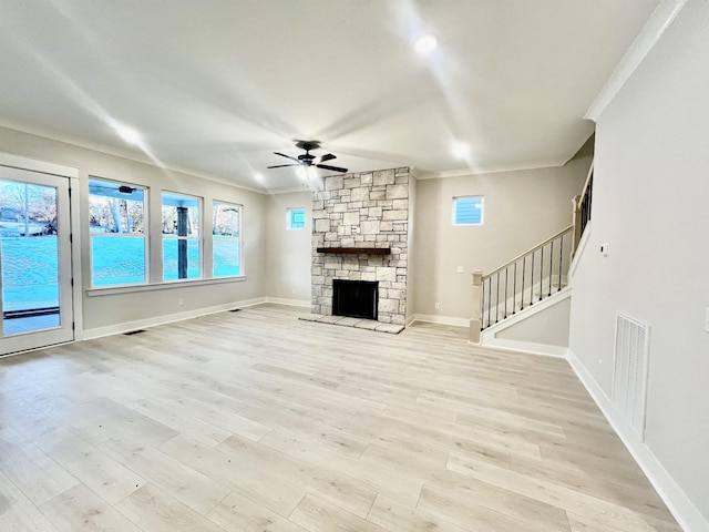 unfurnished living room featuring light wood-type flooring, ceiling fan, a stone fireplace, and ornamental molding