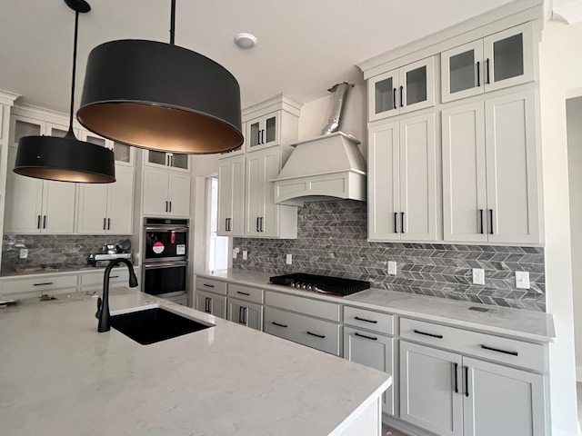 kitchen with tasteful backsplash, hanging light fixtures, stainless steel double oven, sink, and black gas cooktop