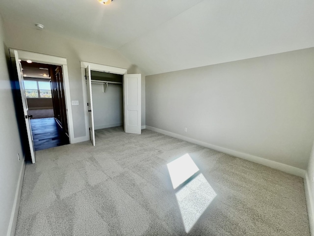 unfurnished bedroom featuring a closet, vaulted ceiling, and light colored carpet