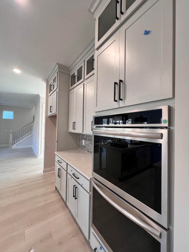 kitchen with white cabinetry, backsplash, stainless steel double oven, and light hardwood / wood-style floors