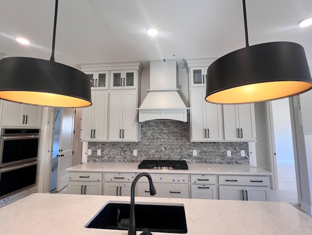 kitchen featuring hanging light fixtures, sink, premium range hood, white cabinets, and backsplash