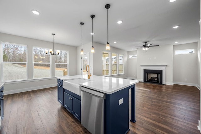 kitchen featuring stainless steel dishwasher, blue cabinets, sink, decorative light fixtures, and an island with sink