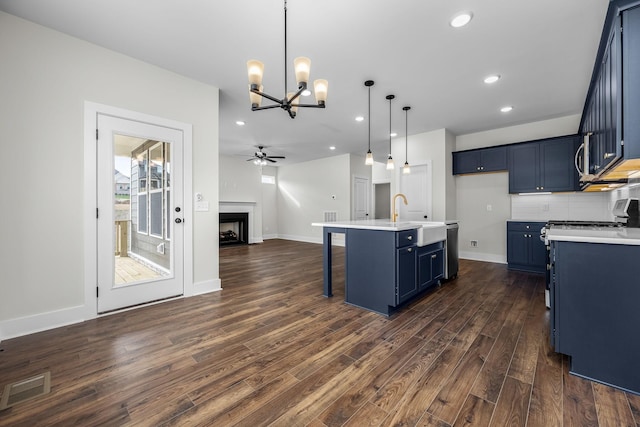 kitchen with blue cabinetry, dishwasher, a kitchen island with sink, pendant lighting, and dark hardwood / wood-style floors