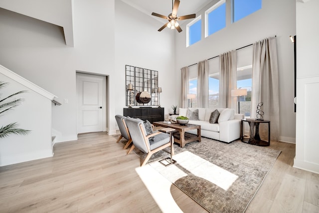 living room with light hardwood / wood-style flooring, ceiling fan, and a high ceiling