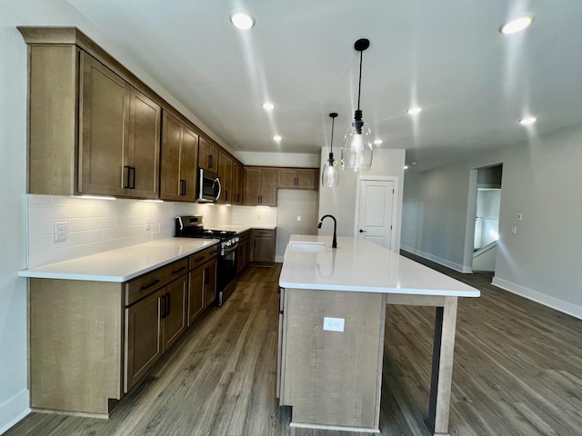 kitchen with sink, appliances with stainless steel finishes, dark hardwood / wood-style floors, an island with sink, and decorative light fixtures