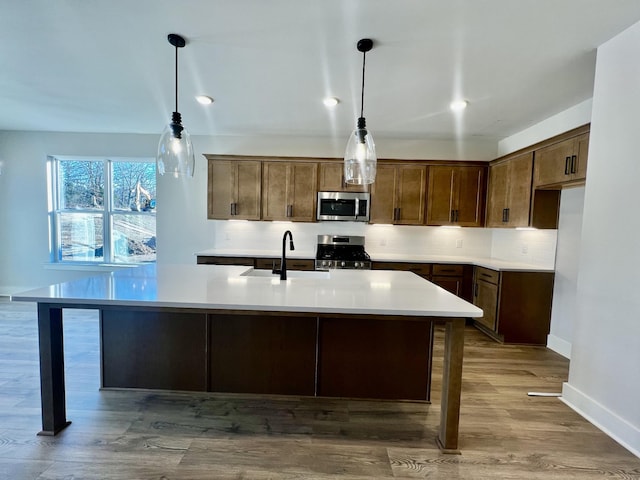 kitchen featuring stainless steel appliances, hanging light fixtures, sink, and light wood-type flooring