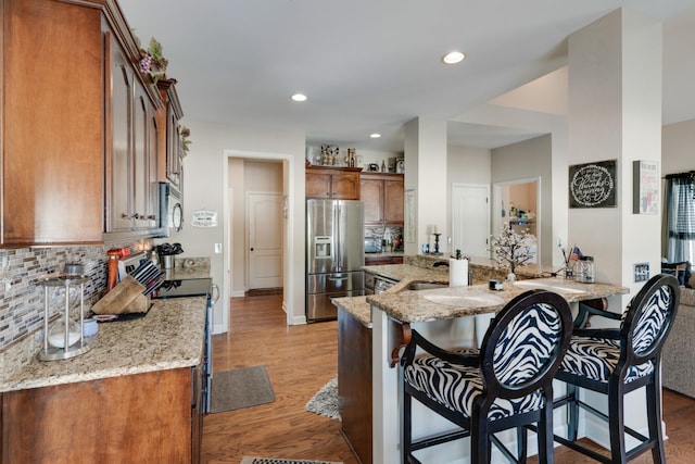 kitchen with light stone countertops, appliances with stainless steel finishes, a kitchen bar, kitchen peninsula, and light wood-type flooring