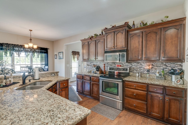 kitchen featuring sink, light stone counters, hanging light fixtures, and appliances with stainless steel finishes