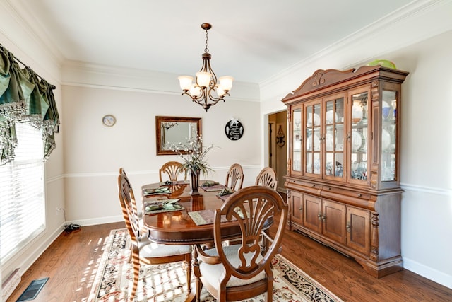 dining room with dark wood-type flooring, plenty of natural light, ornamental molding, and an inviting chandelier