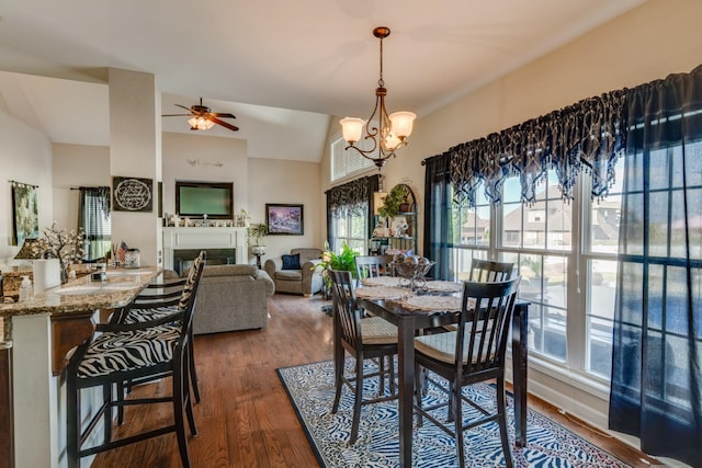 dining space featuring dark wood-type flooring, ceiling fan with notable chandelier, and vaulted ceiling