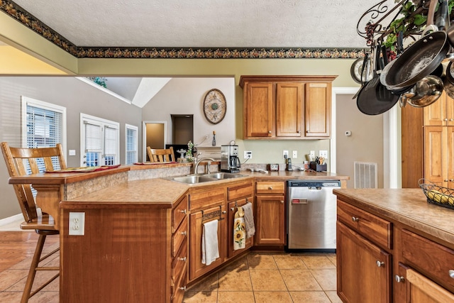 kitchen featuring a textured ceiling, sink, light tile patterned flooring, a breakfast bar, and stainless steel dishwasher