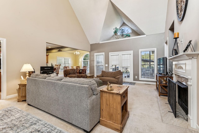 living room with a fireplace, light colored carpet, high vaulted ceiling, and a notable chandelier