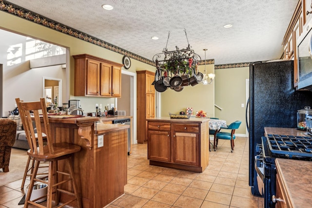 kitchen featuring a kitchen bar, gas range, a textured ceiling, and light tile patterned flooring