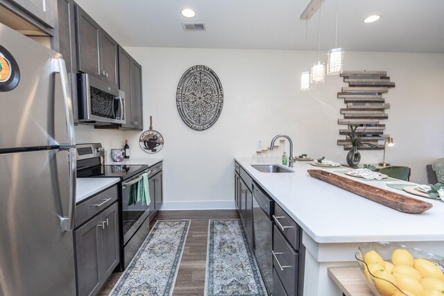 kitchen with pendant lighting, appliances with stainless steel finishes, dark wood-type flooring, sink, and dark brown cabinets