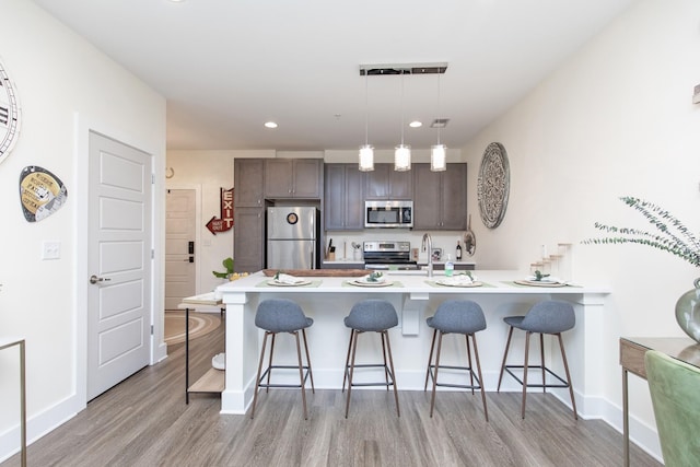 kitchen with light hardwood / wood-style floors, appliances with stainless steel finishes, a kitchen breakfast bar, sink, and decorative light fixtures