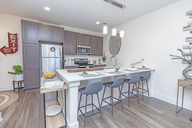 kitchen featuring appliances with stainless steel finishes, dark brown cabinetry, hanging light fixtures, kitchen peninsula, and a breakfast bar area