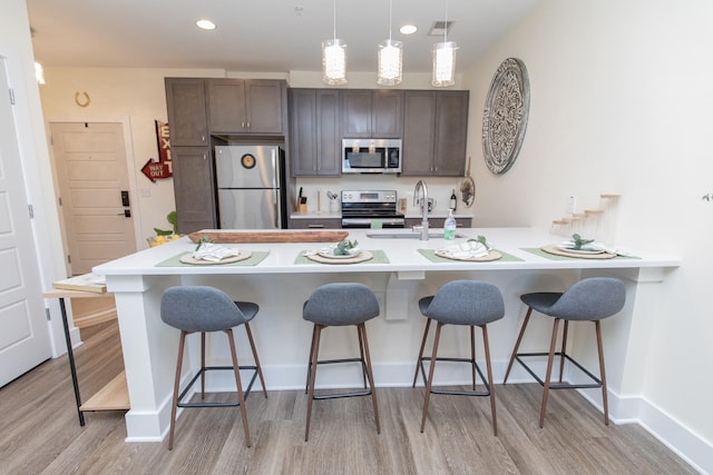 kitchen with pendant lighting, appliances with stainless steel finishes, light hardwood / wood-style floors, sink, and a breakfast bar