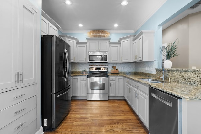 kitchen with wood-type flooring, appliances with stainless steel finishes, sink, white cabinetry, and ornamental molding