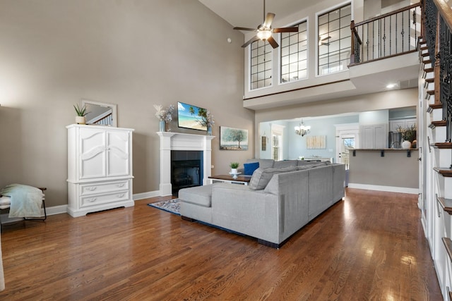 living room featuring a towering ceiling, ceiling fan, dark hardwood / wood-style flooring, and a tiled fireplace