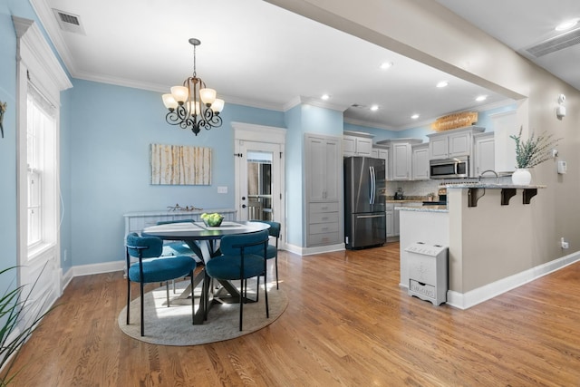 dining area with ornamental molding, a chandelier, and light hardwood / wood-style flooring