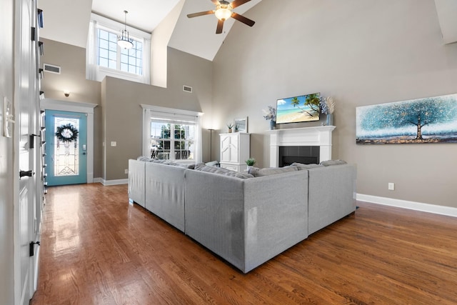 living room featuring ceiling fan, high vaulted ceiling, dark wood-type flooring, and a tiled fireplace