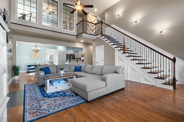 living room with hardwood / wood-style floors, ceiling fan with notable chandelier, and a high ceiling