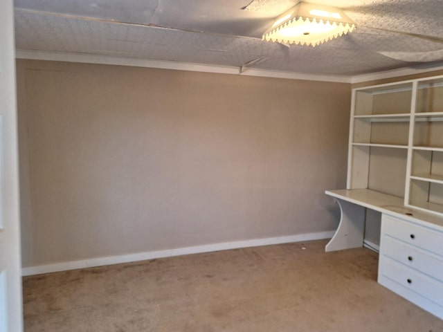 unfurnished office with built in desk, light colored carpet, and crown molding