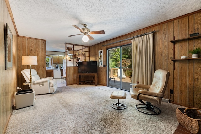 carpeted living room with ornamental molding, ceiling fan, and wooden walls