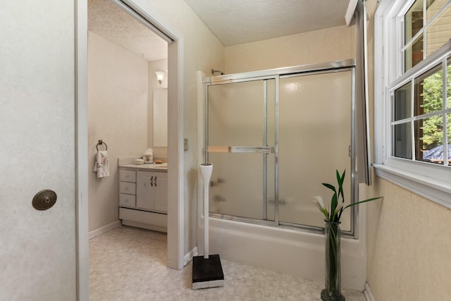 bathroom with a textured ceiling, shower / bath combination with glass door, and vanity