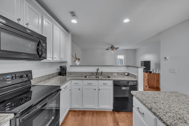 kitchen with sink, light wood-type flooring, white cabinets, light stone countertops, and black appliances