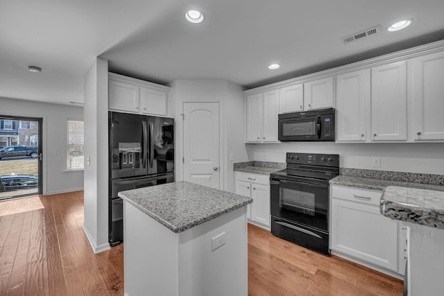 kitchen featuring light stone countertops, white cabinets, black appliances, a center island, and light wood-type flooring