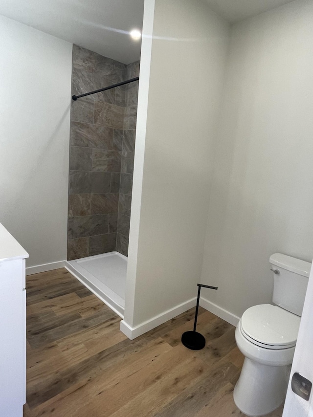 bathroom featuring wood-type flooring, toilet, and a tile shower