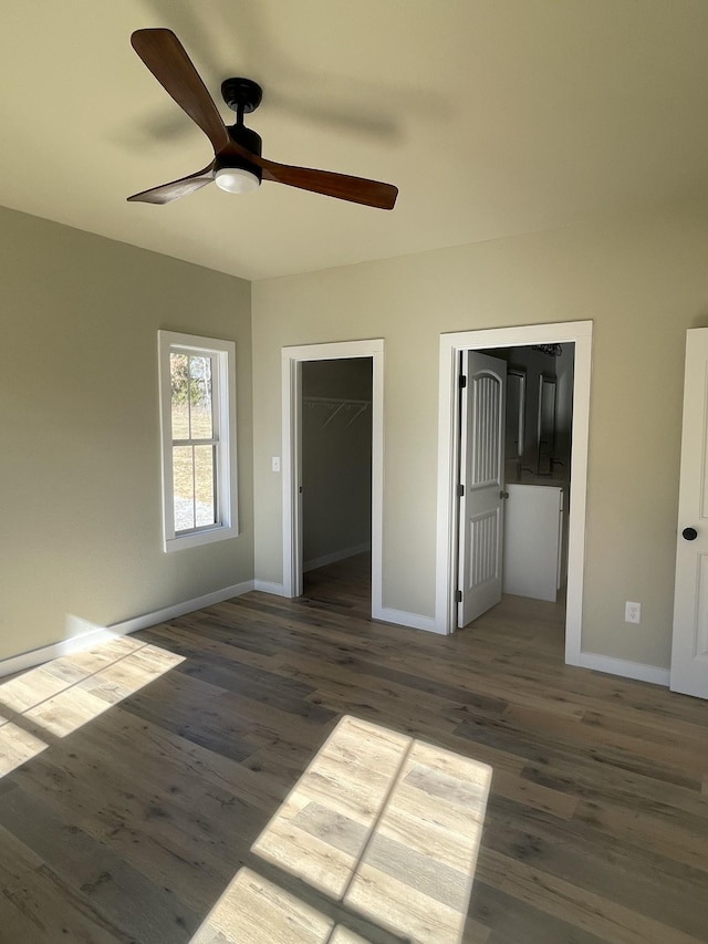 unfurnished bedroom with ceiling fan, dark wood-type flooring, a spacious closet, and a closet