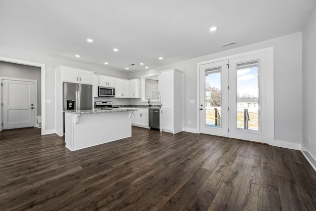 kitchen with white cabinets, a kitchen island, dark wood-type flooring, stainless steel appliances, and light stone counters