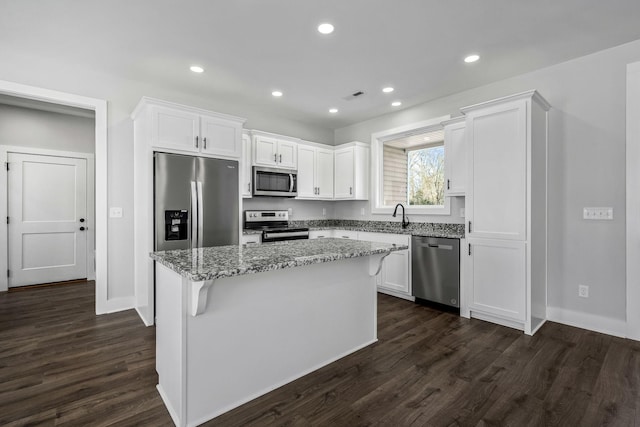 kitchen with light stone countertops, appliances with stainless steel finishes, dark hardwood / wood-style floors, and a kitchen island