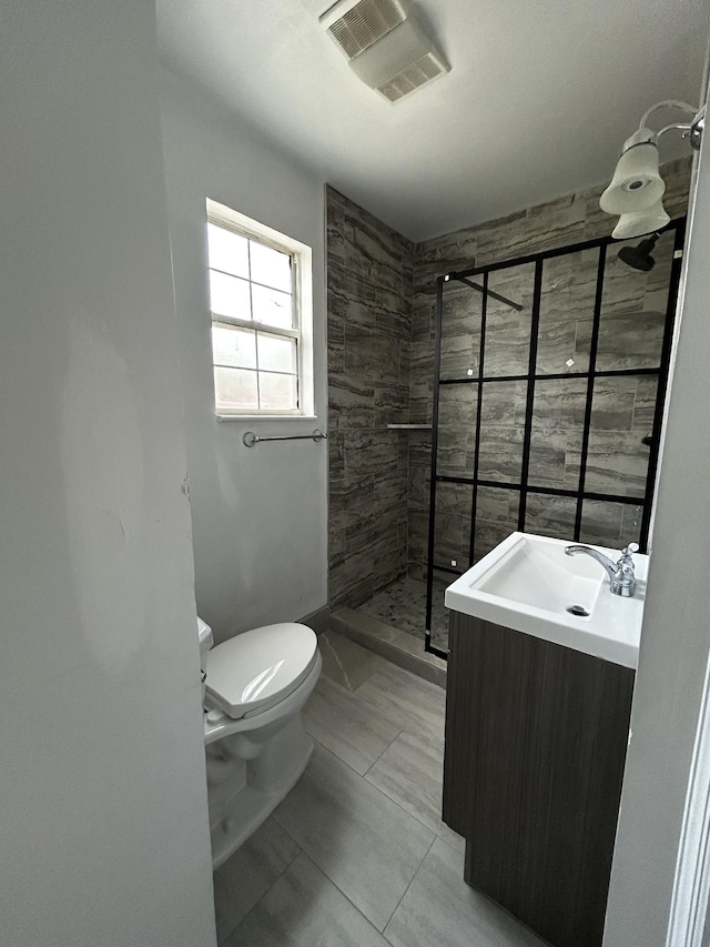 bathroom with tiled shower, toilet, tile patterned flooring, and vanity