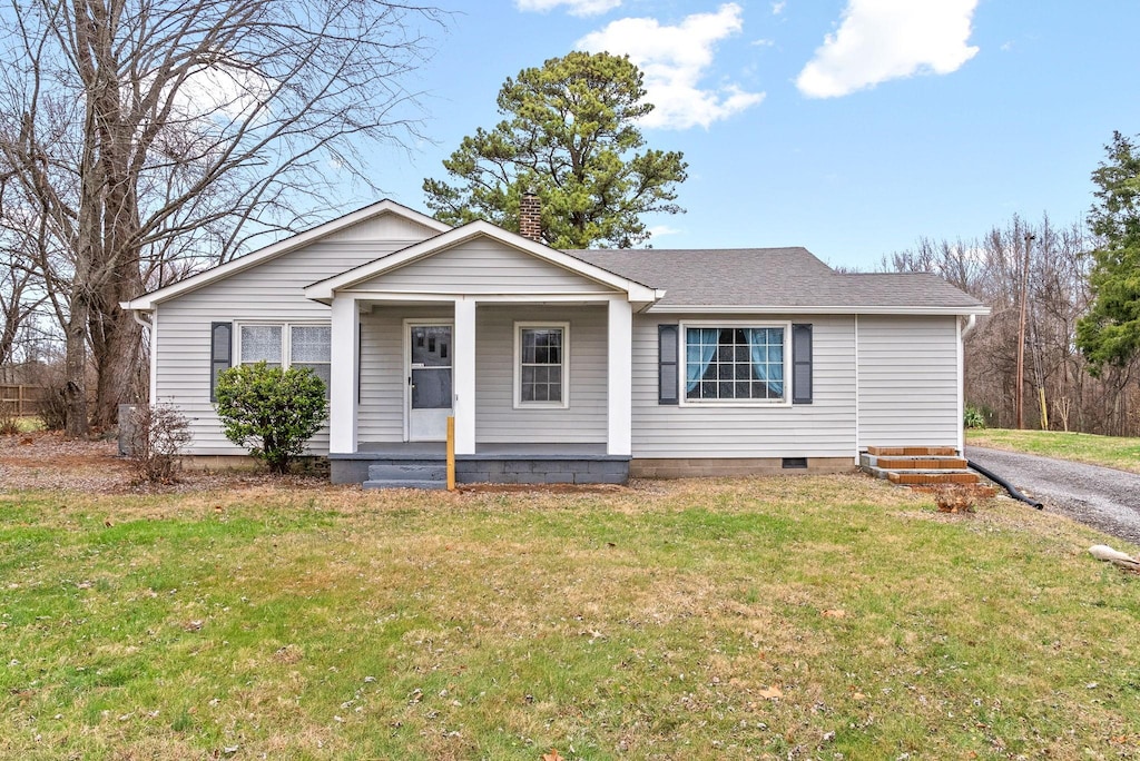 view of front of home with a shingled roof, covered porch, a chimney, and a front lawn