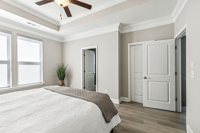 bedroom with hardwood / wood-style floors, a closet, ceiling fan, a tray ceiling, and crown molding