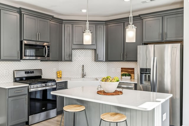 kitchen featuring tasteful backsplash, gray cabinetry, sink, decorative light fixtures, and stainless steel appliances