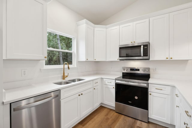 kitchen with sink, white cabinets, vaulted ceiling, and stainless steel appliances