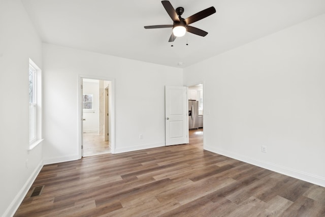 unfurnished bedroom featuring ceiling fan, connected bathroom, dark hardwood / wood-style floors, and stainless steel fridge