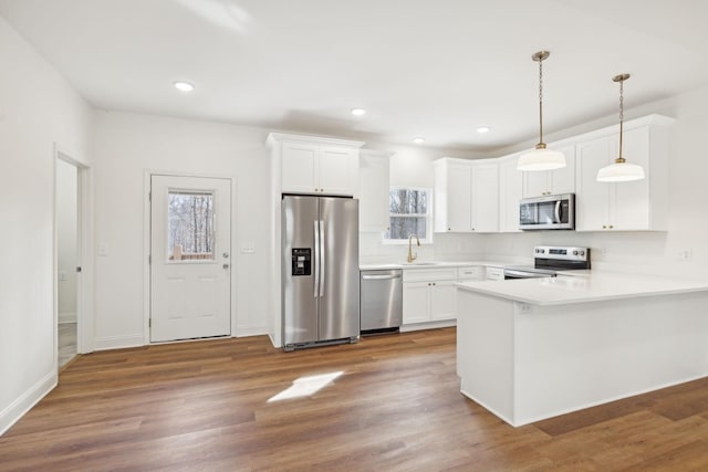 kitchen with appliances with stainless steel finishes, hanging light fixtures, white cabinets, kitchen peninsula, and dark hardwood / wood-style flooring