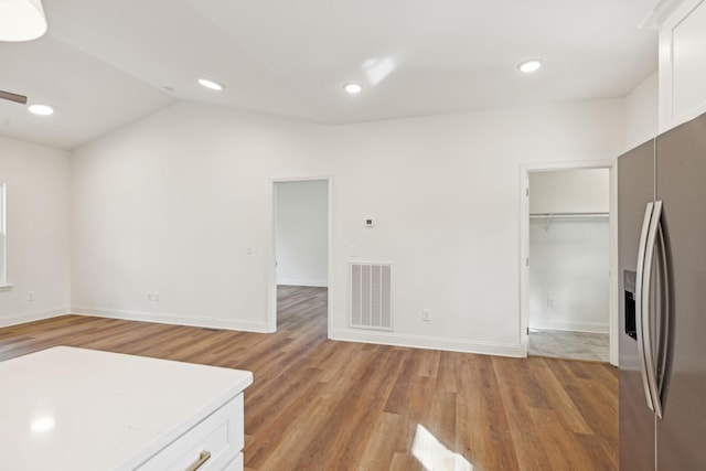 kitchen with white cabinets, vaulted ceiling, hardwood / wood-style floors, and stainless steel refrigerator with ice dispenser