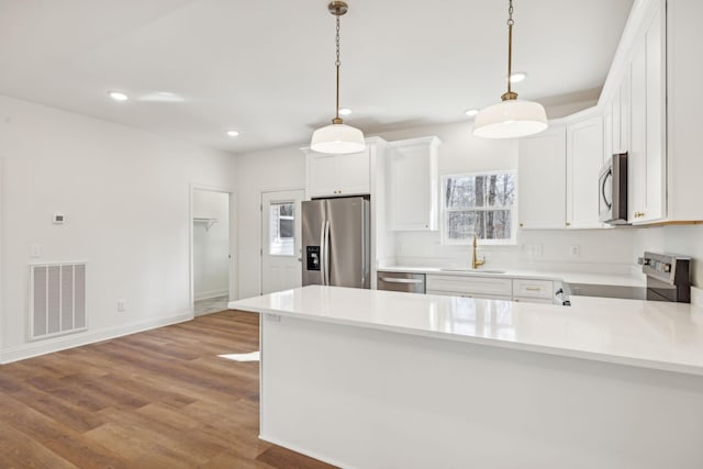 kitchen featuring appliances with stainless steel finishes, sink, decorative light fixtures, white cabinets, and light wood-type flooring