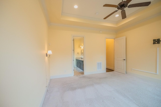 unfurnished bedroom featuring crown molding, connected bathroom, light colored carpet, and a tray ceiling