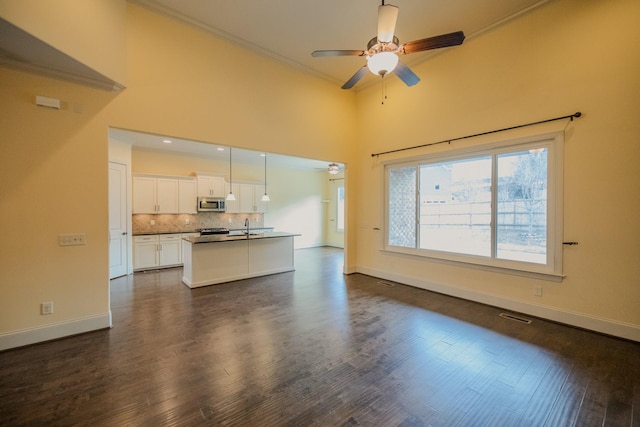 unfurnished living room featuring dark wood-type flooring, sink, ornamental molding, a towering ceiling, and ceiling fan