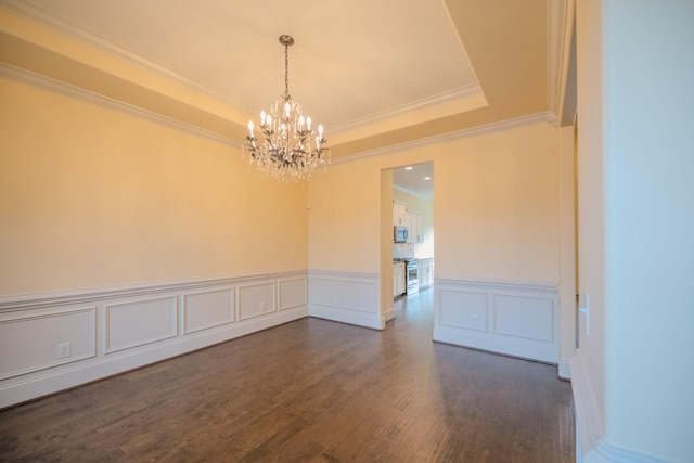 empty room with a chandelier, ornamental molding, dark hardwood / wood-style floors, and a raised ceiling