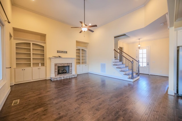 unfurnished living room with built in features, ornamental molding, ceiling fan, a brick fireplace, and dark wood-type flooring