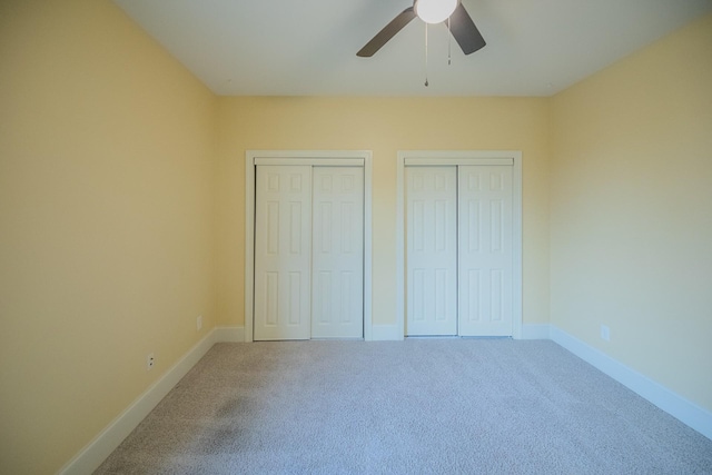 unfurnished bedroom featuring two closets, carpet floors, and ceiling fan